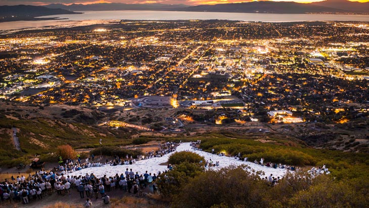 A group of students gathered around the Y on Y Mountain overlooking Utah Valley in the evening