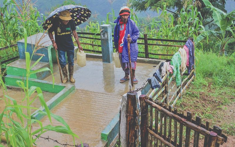 Photo of two women standing outside on a deck filling plastic water jugs from a clean water well.