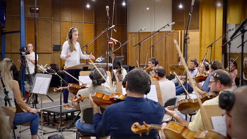 Young woman college student leading orchestra in a music studio