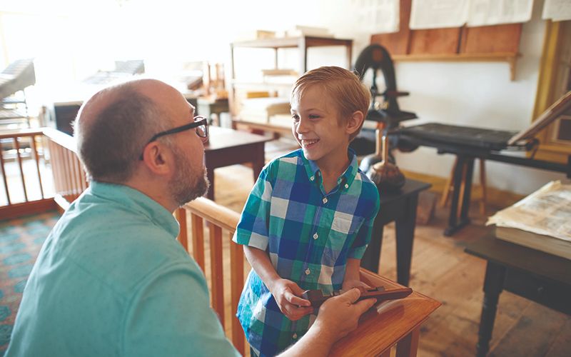 Photo of a father and son inside a replica of the printing press building. 