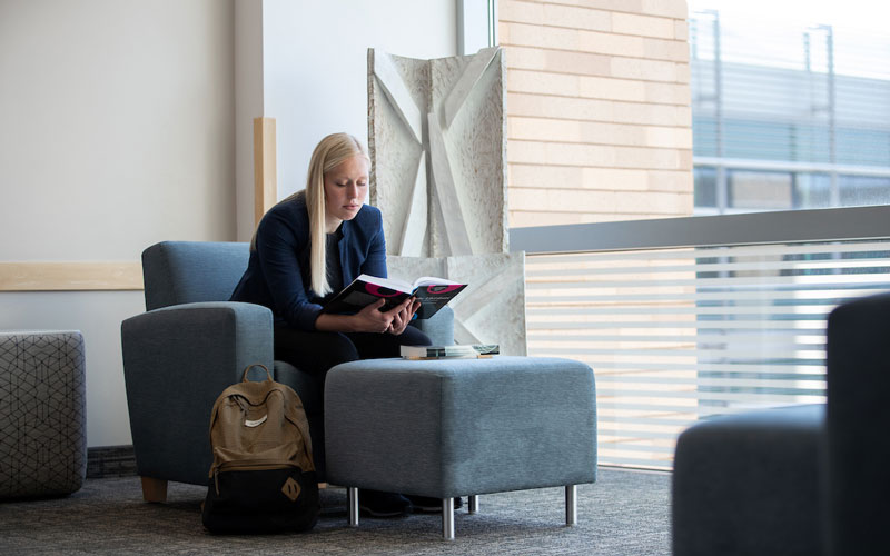 Female student in lounge chair reading textbook.