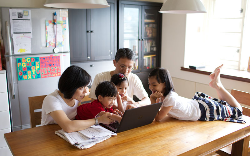 family sitting at a kitchen table looking at family history on a laptop