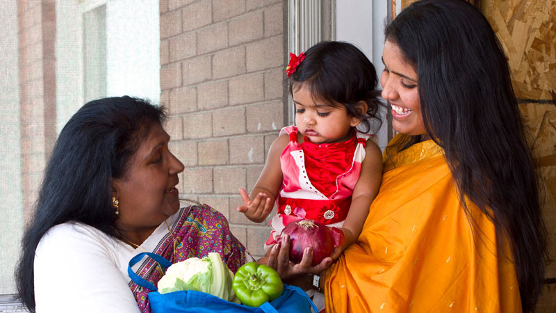 Woman giving a bag of groceries to another woman who is holding her child.