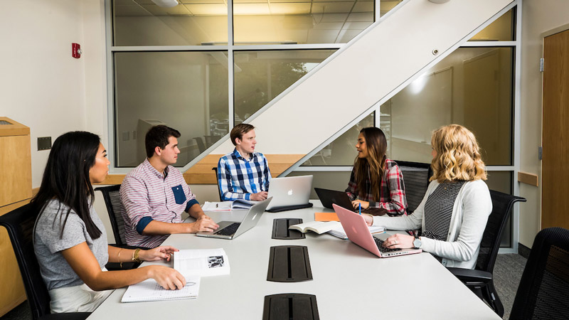 Five BYU Marriott School of Business students seated around a conference room table discussing.