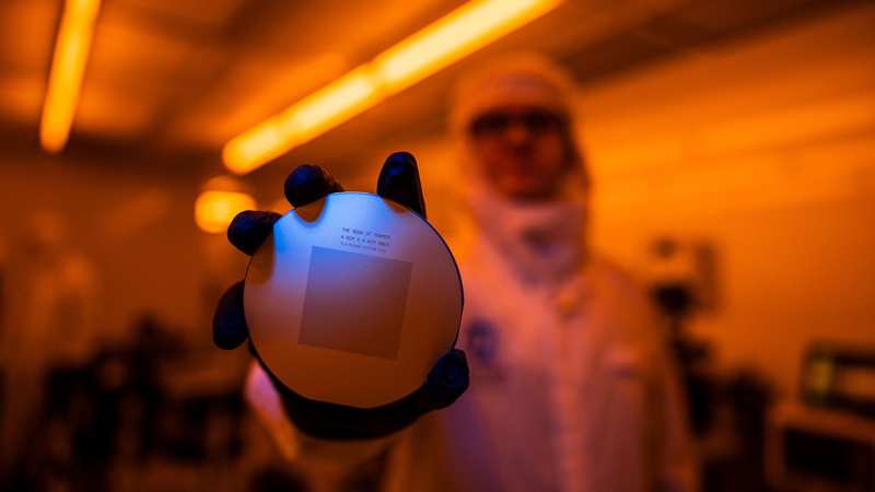 BYU student holding up a silicon disc, or wafer, with the Book of Mormon etched on it.