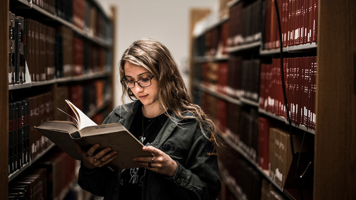 Female student in library reading textbook.