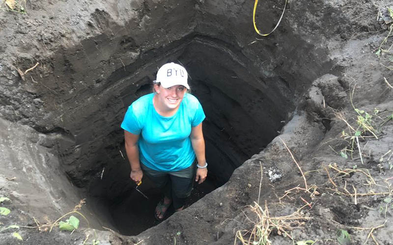 Student with trowel standing in a deep trench