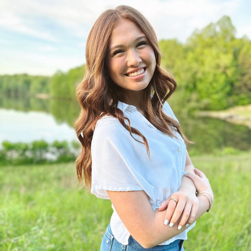 Reagan Vehar outside with green grass, a pond, and trees behind her