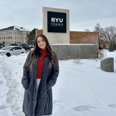 Female BYU-Idaho student standing in the snow with BYU-Idaho sign behind her on campus