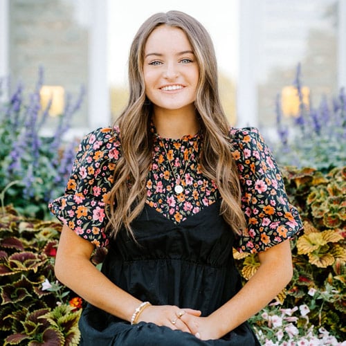 Female BYU-Idaho student smiling with flowers behind her