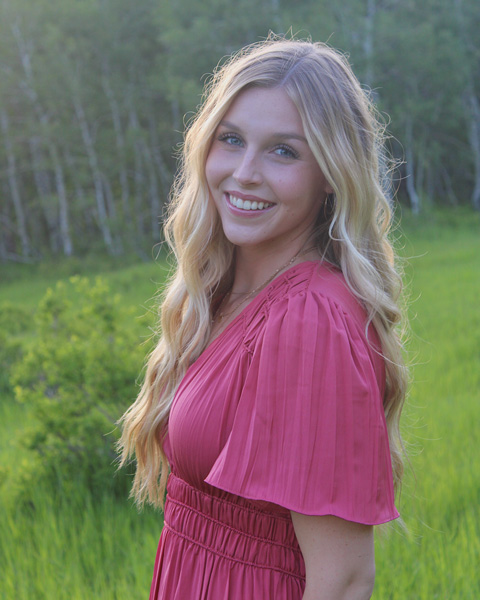 Female college student in pink dress with trees behind.