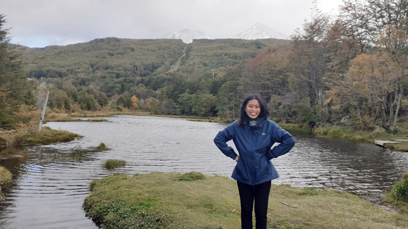 Sister Sariah Resolme in a jacket with her missionary name tag outdoors by a river