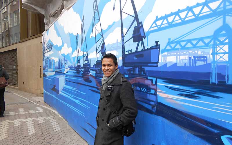 Winston as a missionary poses in front of a painted wall.