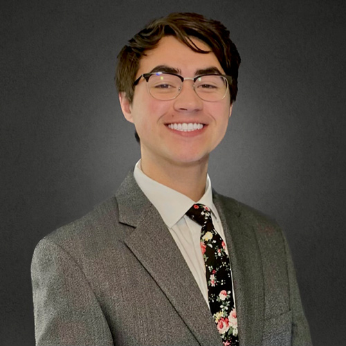 A man smiling wearing a blazer and tie.