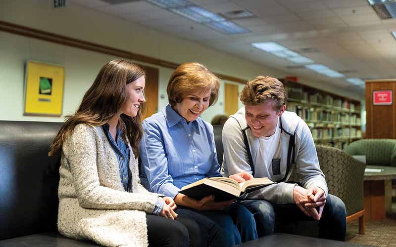 Judy Garvin reads a book with two students in the Harold B. Lee Library.