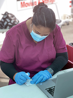 A woman wearing nurse scrubs and a mask and processing a COVID test.