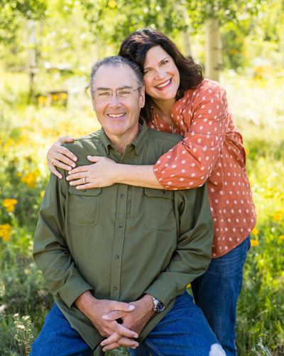 Elderly man and woman, with the woman’s arms around the man.