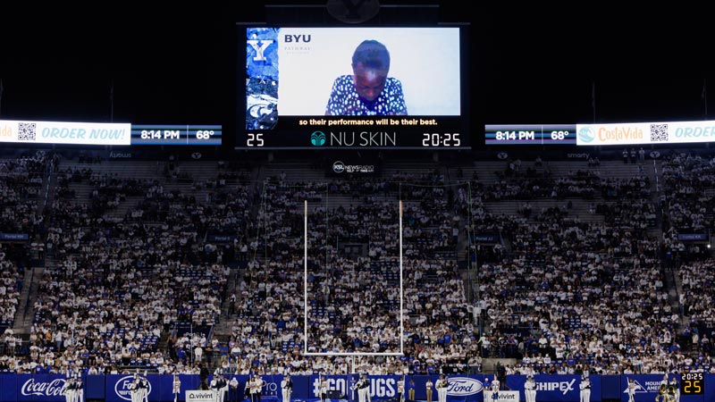 An African women saying a prayer on the jumbotron of a large football stadium.