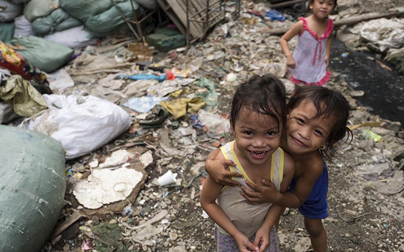 Children playing in garbage smile at the camera