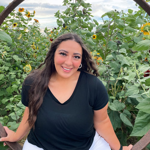 Ensign College student, Sarah Schmitz, smiling while in a sunflower patch on a sunny day. 