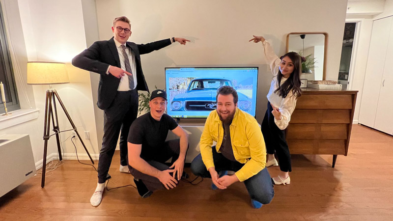 BYU students posing with their award-winning commercial playing on a TV behind them.