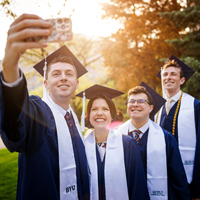 Group of four BYU graduates in their graduation robes taking a selfie