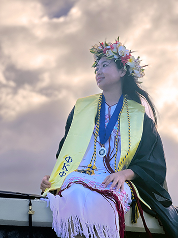 Burmese women wearing graduation robes with tropical flowers in her hair.